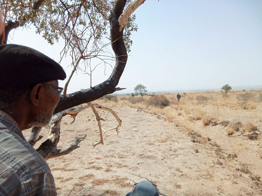 Ein Mann sitzt in einer W&uuml;stenlandschaft, in einiger Entfernung l&auml;uft ein anderer Mann