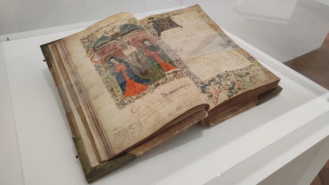 Aufgeschlagenes, altes Buch mit farbiger Illustration und handschriftlichem Text, pr&auml;sentiert in einer Vitrine
