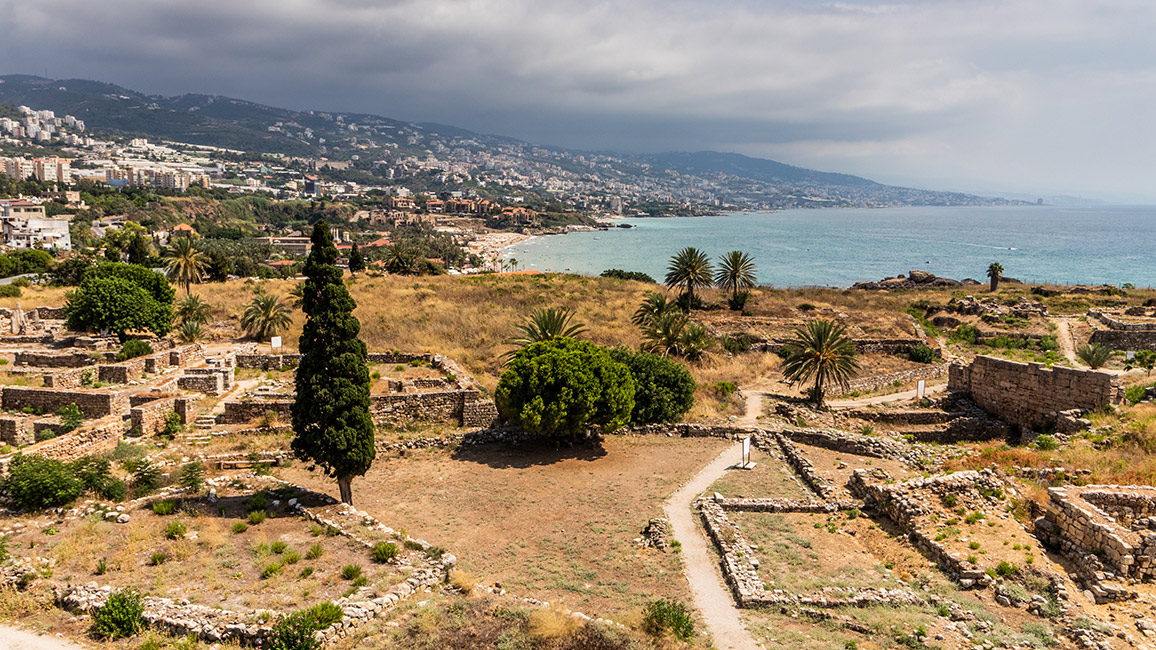 View of archaeological ruins by the coast with mountains in the background and sea on the right
