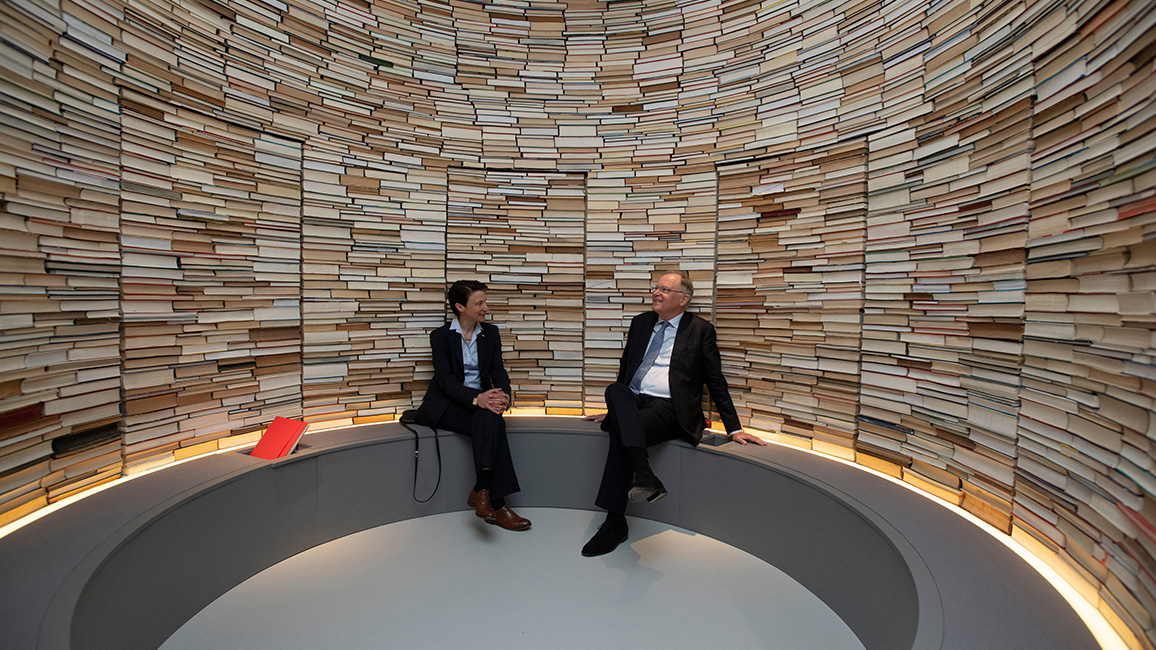 Zwei Personen inmitten eines Turms aus B&uuml;chern