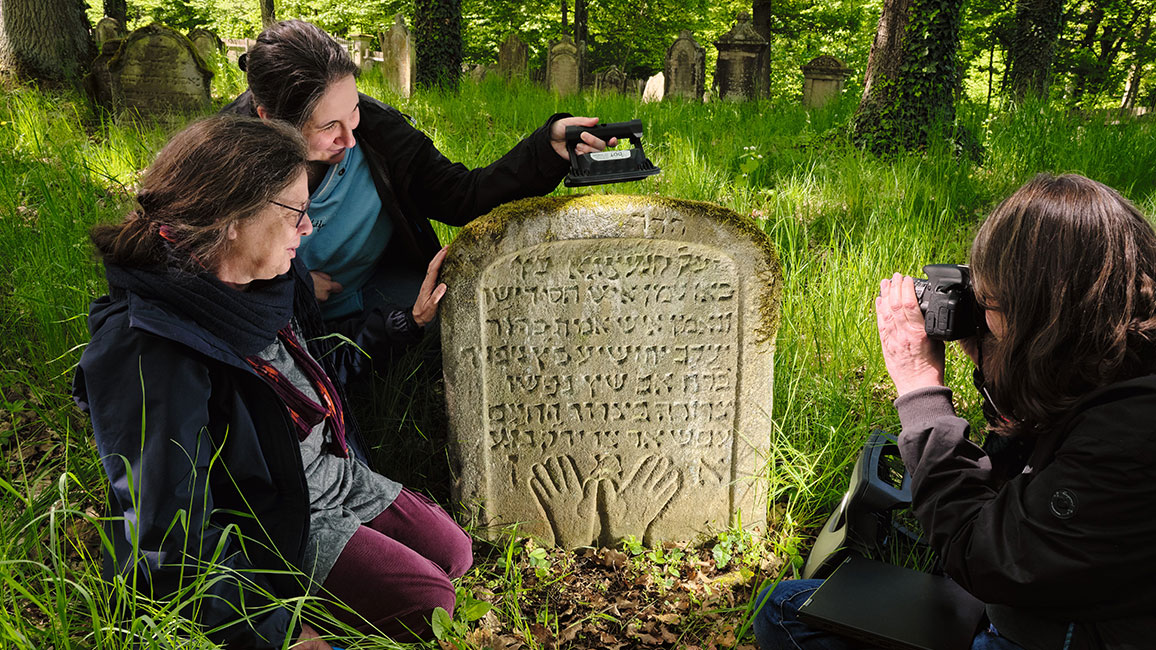 Drei Frauen beleuchten eine Inschrift mit einer Lampe