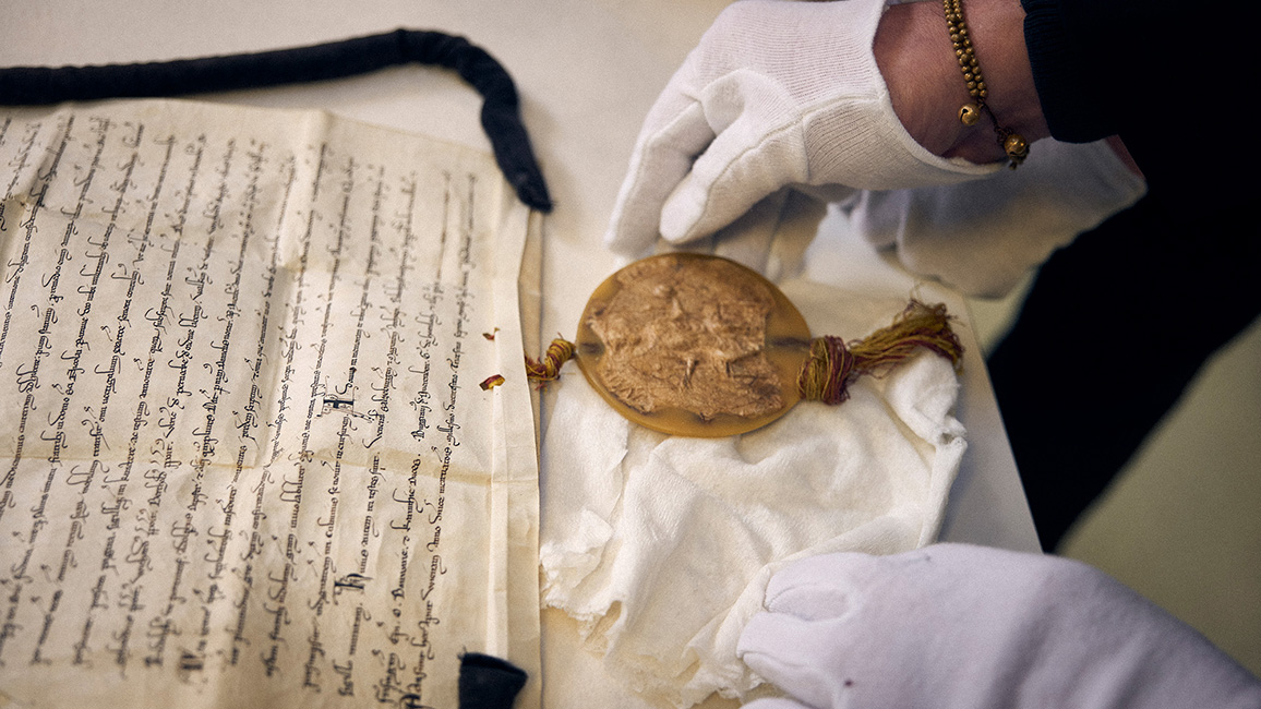Urkunde mit Wachssiegel und eine Hand in wei&szlig;en Handschuhen, die das Schriftst&uuml;ck untersicht