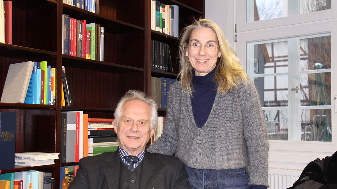 Ein Mann sitzt und eine Frau steht neben einem B&uuml;cherregal